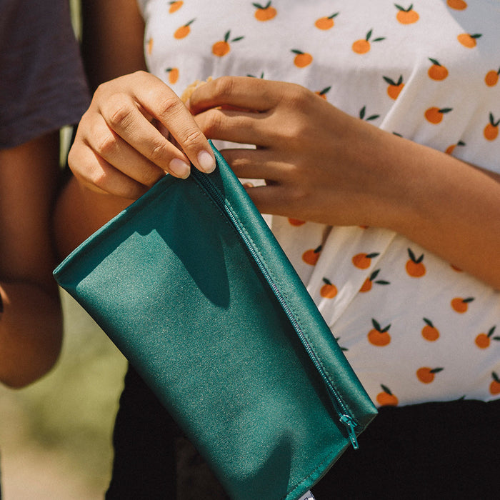 Gros plan sur les mains d'une jeune femme avec un chandail à motif d'oranges qui tient un sac à collation en tissu vert uni dans ses mains